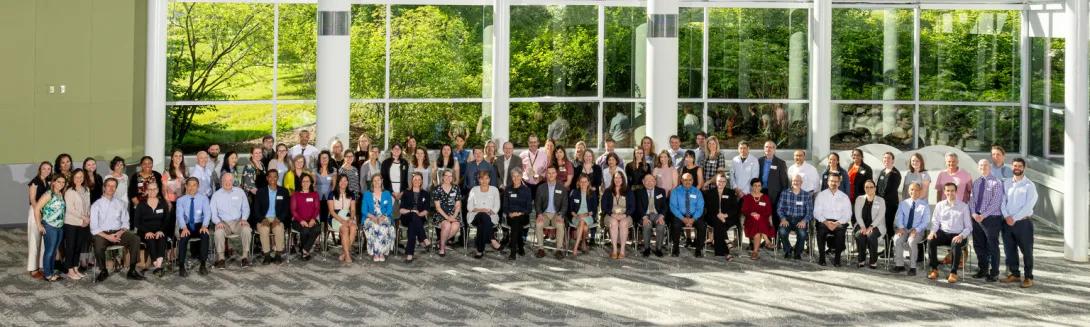 A large group of general medicine professionals stand together on and smiling for a group photo.