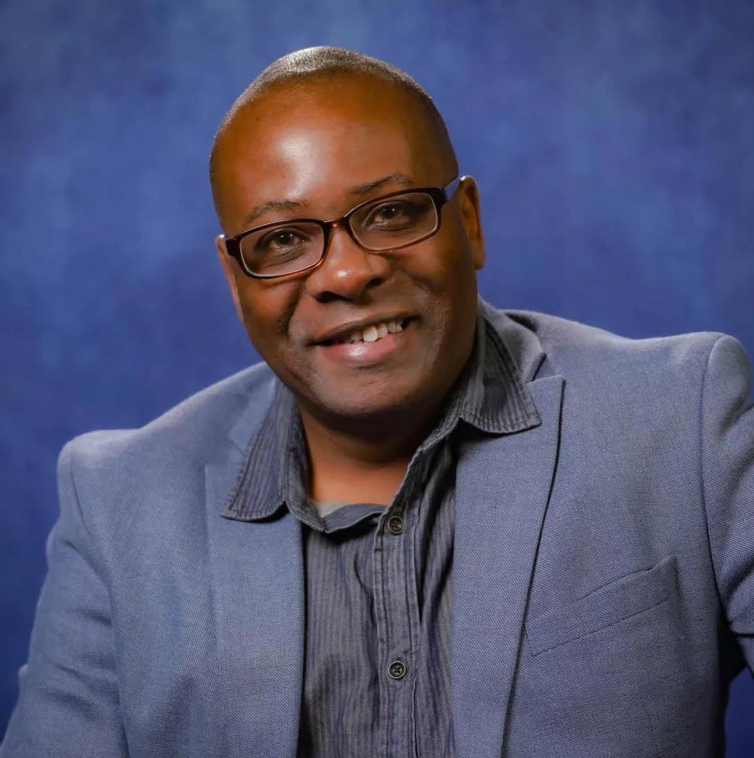 a Black man wearing a grey suit on a blue background 
