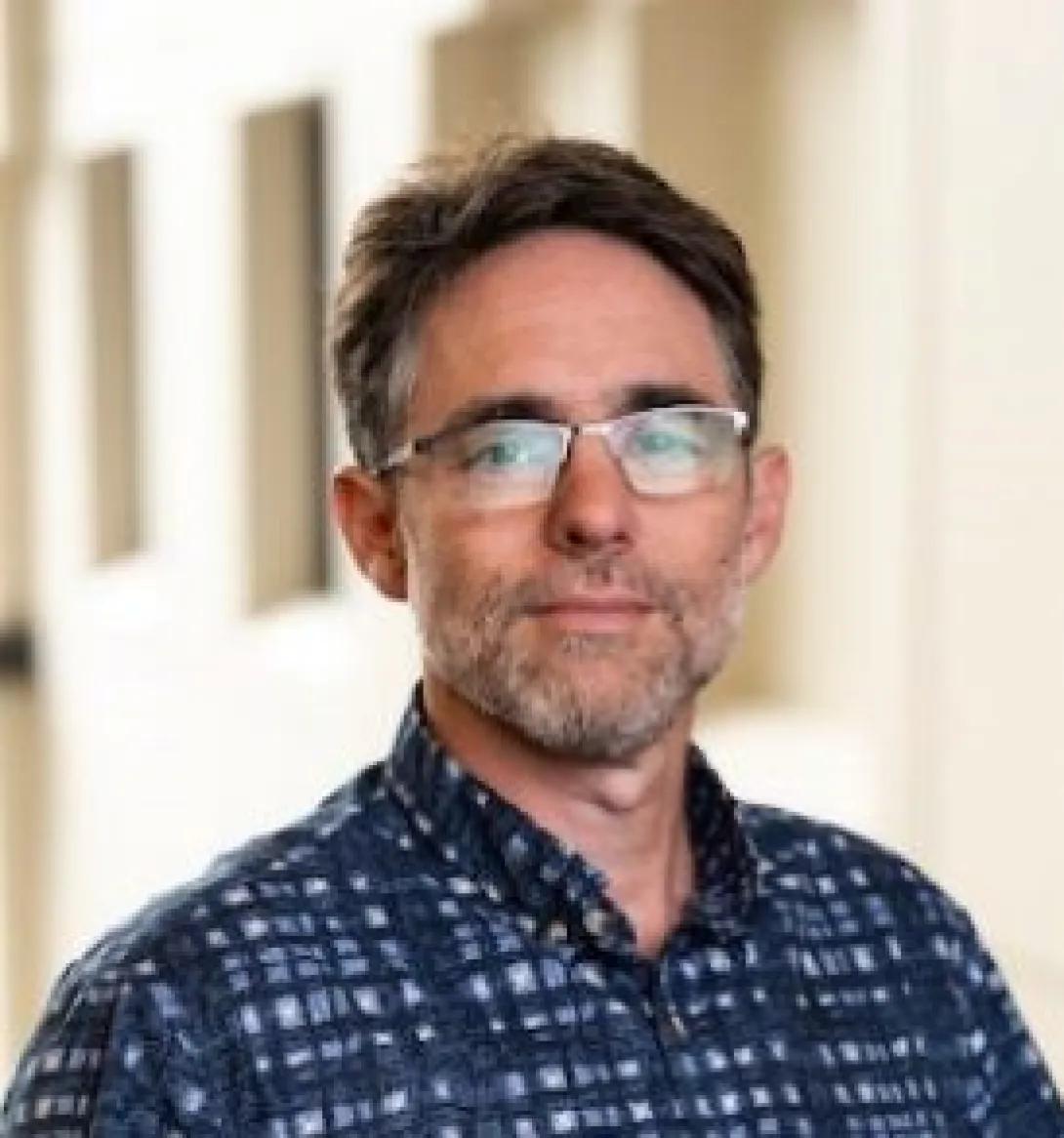 a man with short hair, glasses, and a blue shirt 