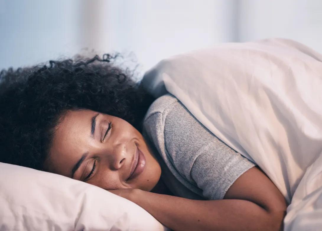 a women with darker skin and curly hair in bed sleeping with the covers wrapped around her