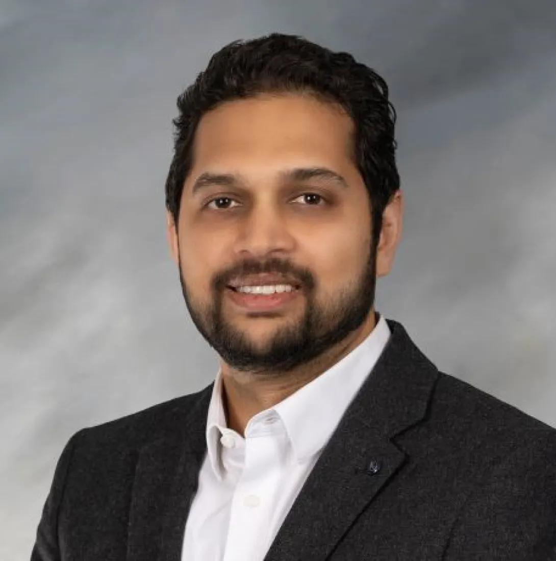 a Middle Eastern man with dark hair and beard wearing a suit 