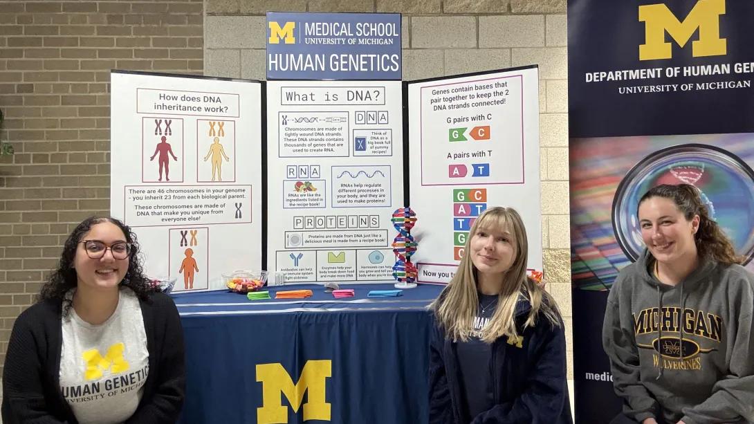 Students in front of a table and poster explaining human genetics