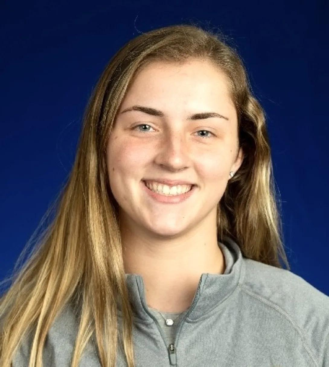 Image of a person with long dark blonde hair wearing a gray shirt on a dark blue background