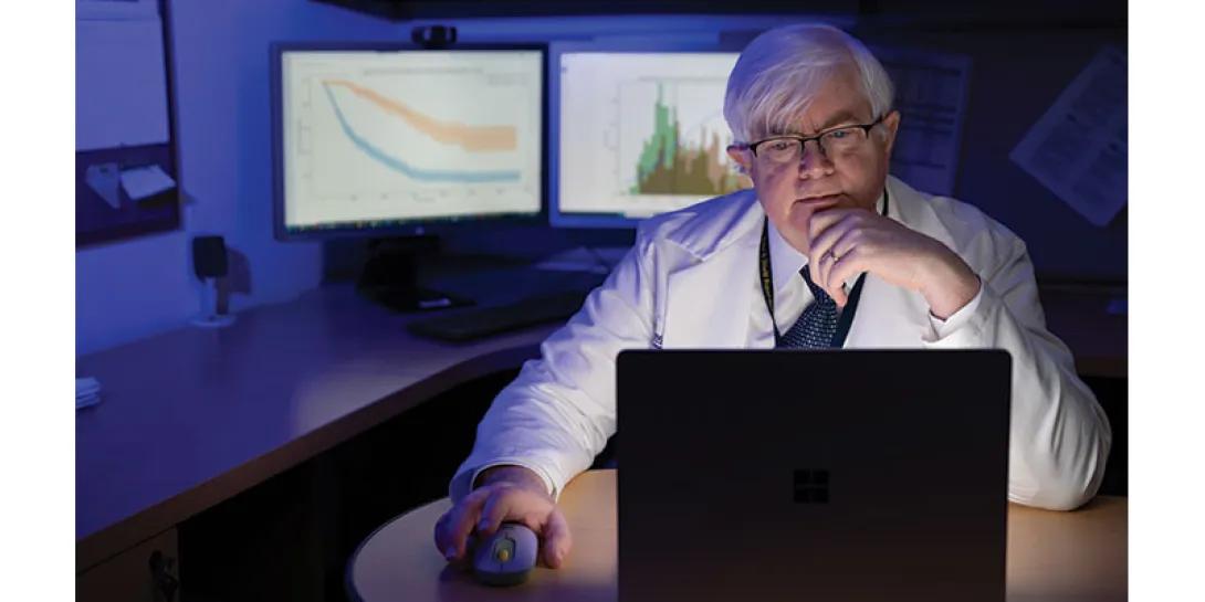 Dr. Charles Mayo sits in front of a computer analyzing patient data
