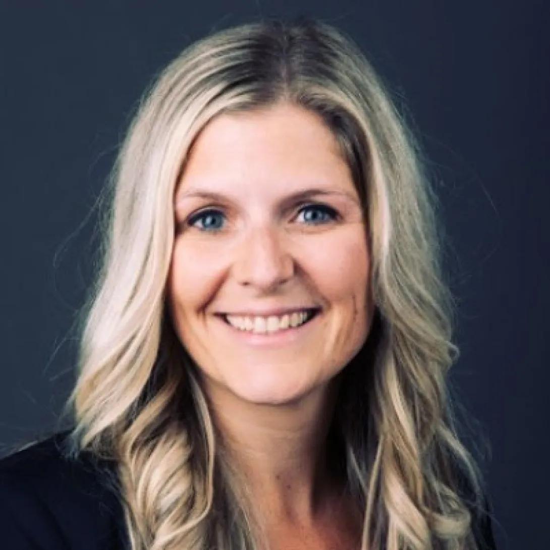 Smiling woman with blond hair in front of a dark grey background