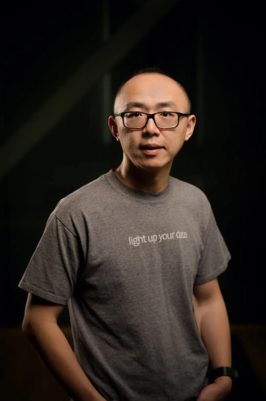 Man with glasses and a grey tshirt in front of a black background