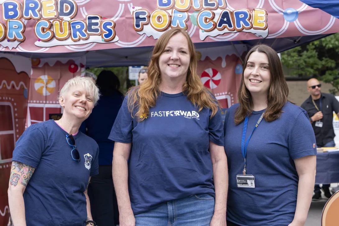 three people posing for a photo at a tabling event outdoors
