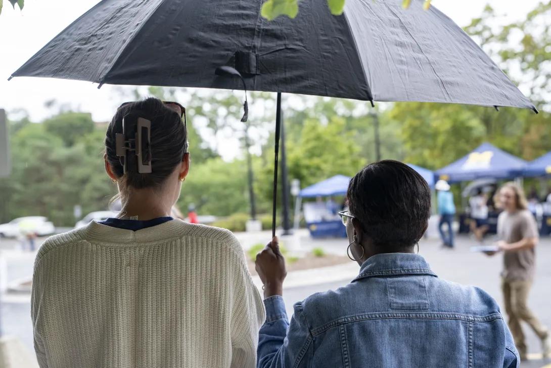 two people holding an umbrella at a tabling event outdoors