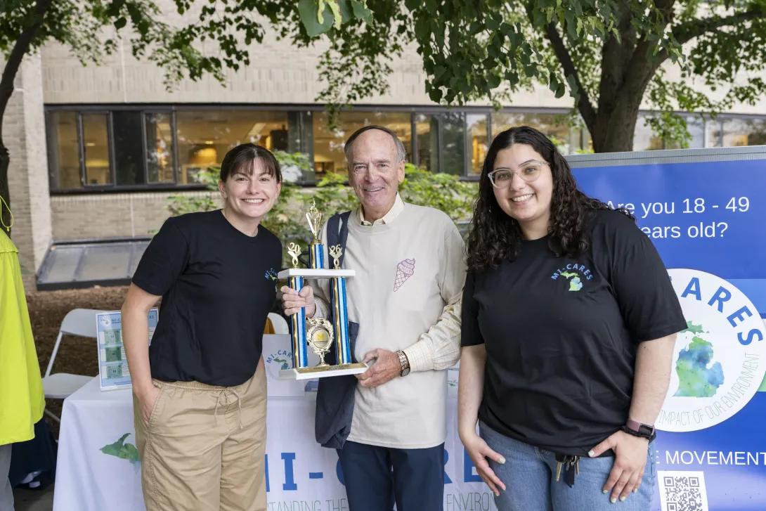 three people posing for a photo at a tabling event outdoors
