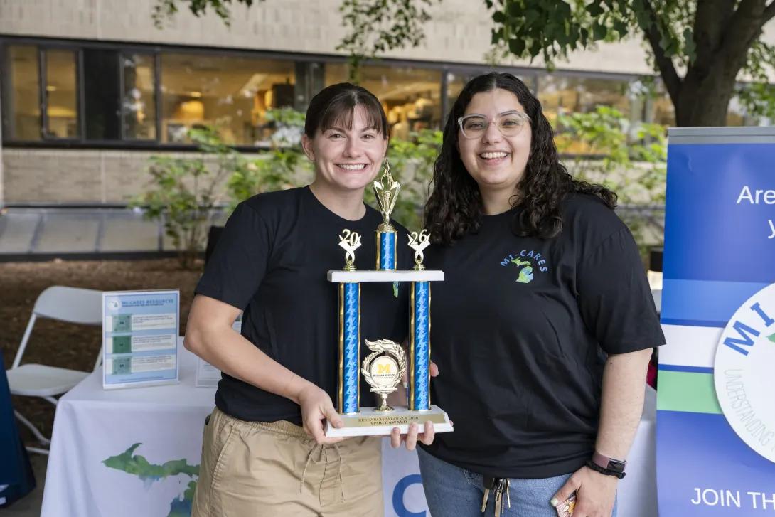 two people holding a trophy and posing for a photo at a tabling event outdoors