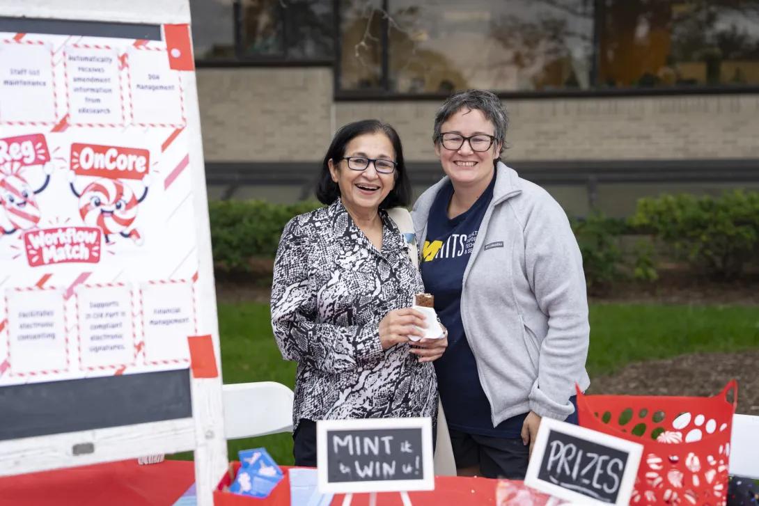 two people posing for a photo at a tabling event outdoors