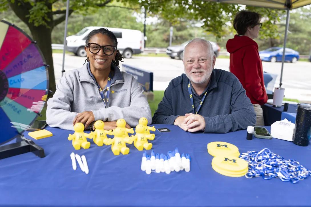 two people posing for a photo at a tabling event outdoors