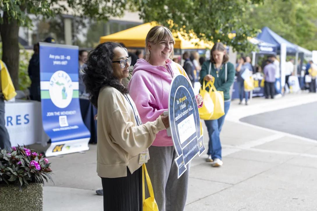group of people posing for a photo and holding a sign at a tabling event outdoors