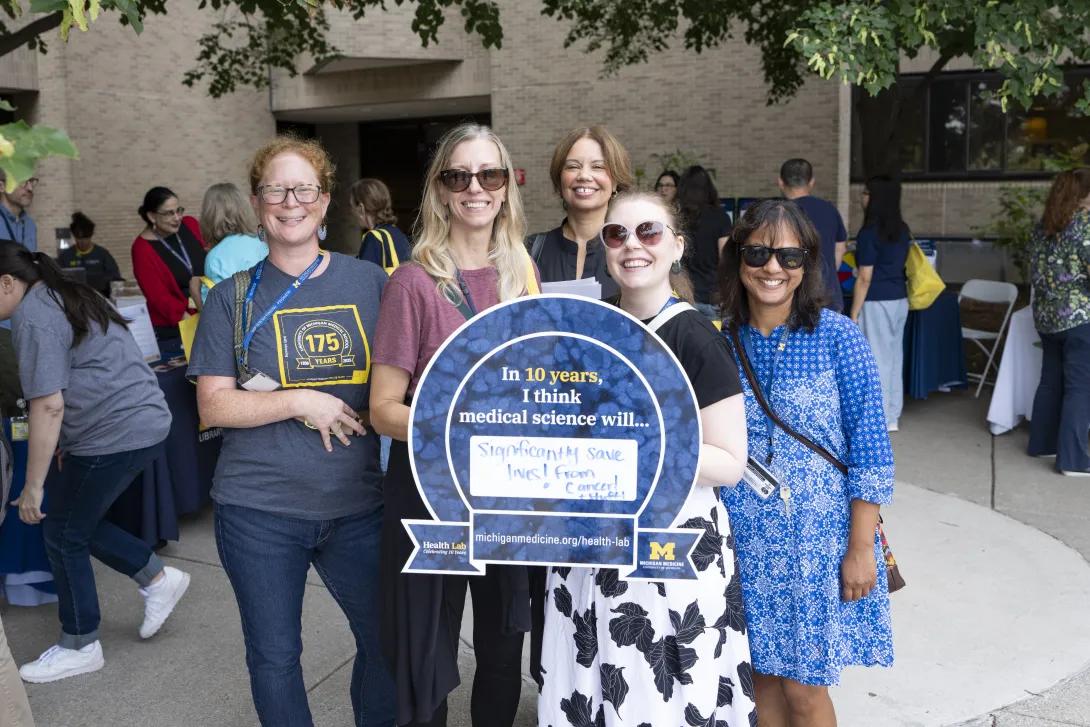 group of people posing for a photo and holding a sign at a tabling event outdoors