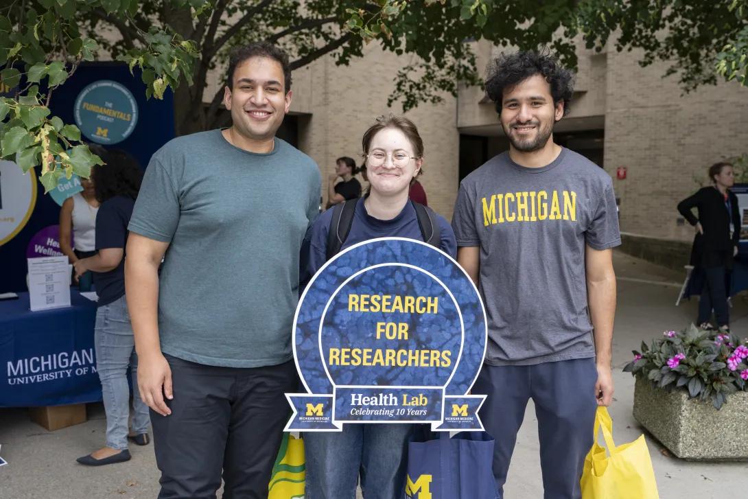 group of people posing for a photo and holding a sign at a tabling event outdoors