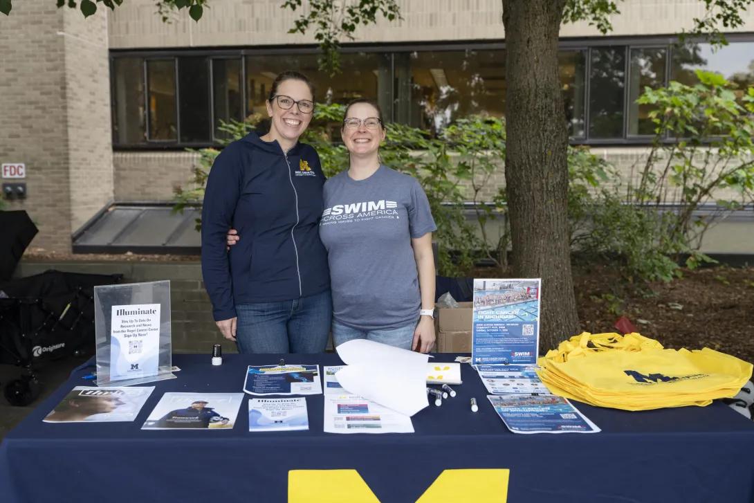 two people posing for a photo at a tabling event outdoors