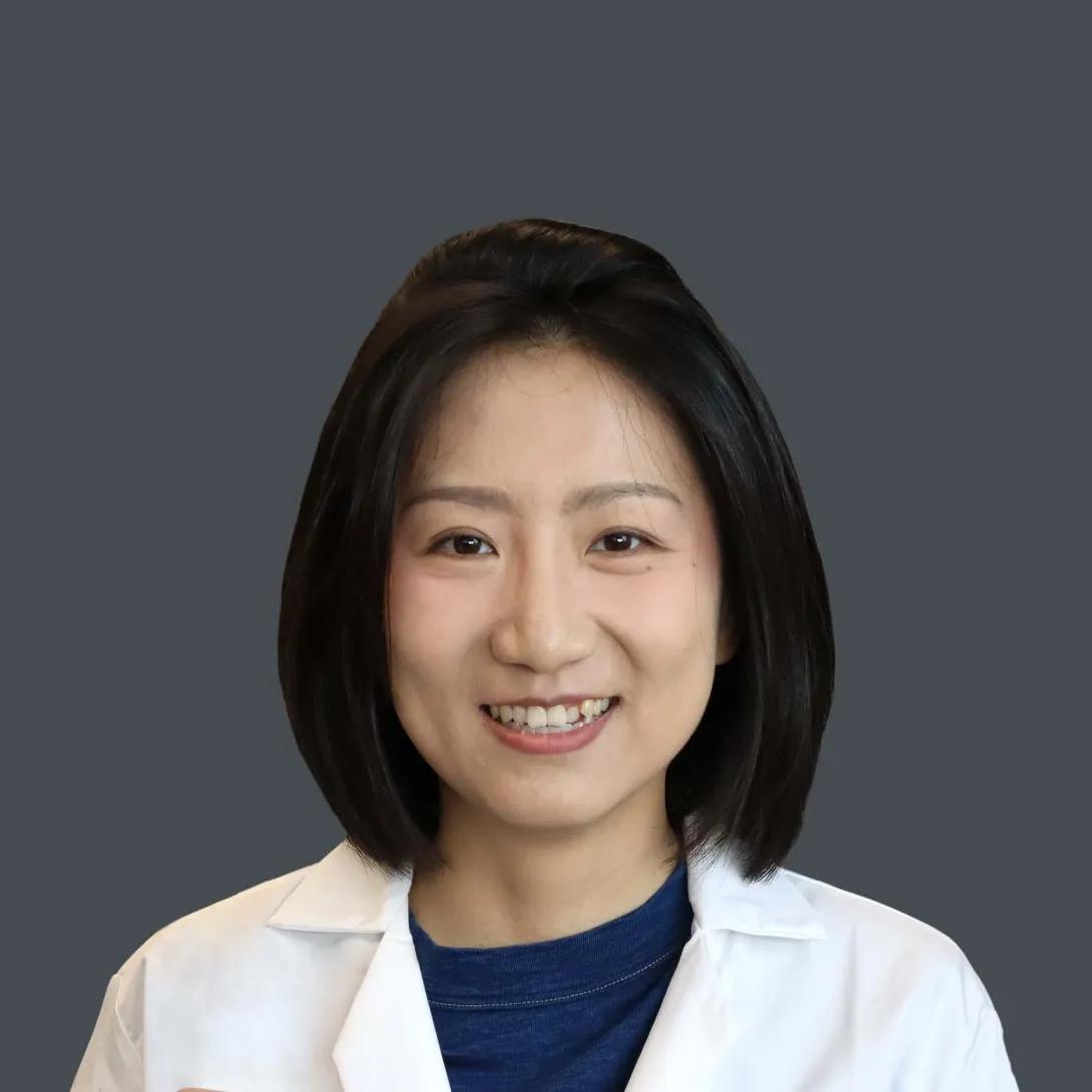 Woman with short black hair smiles wearing a white lab coat