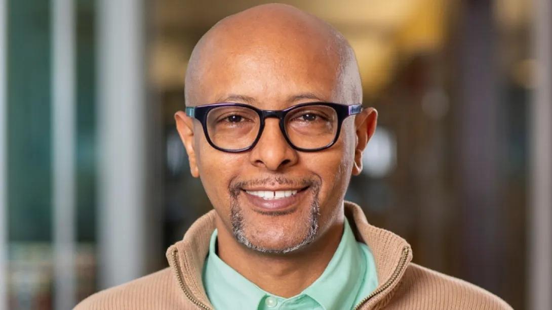 Man with glasses and grey beard smiles in front of a blurred background